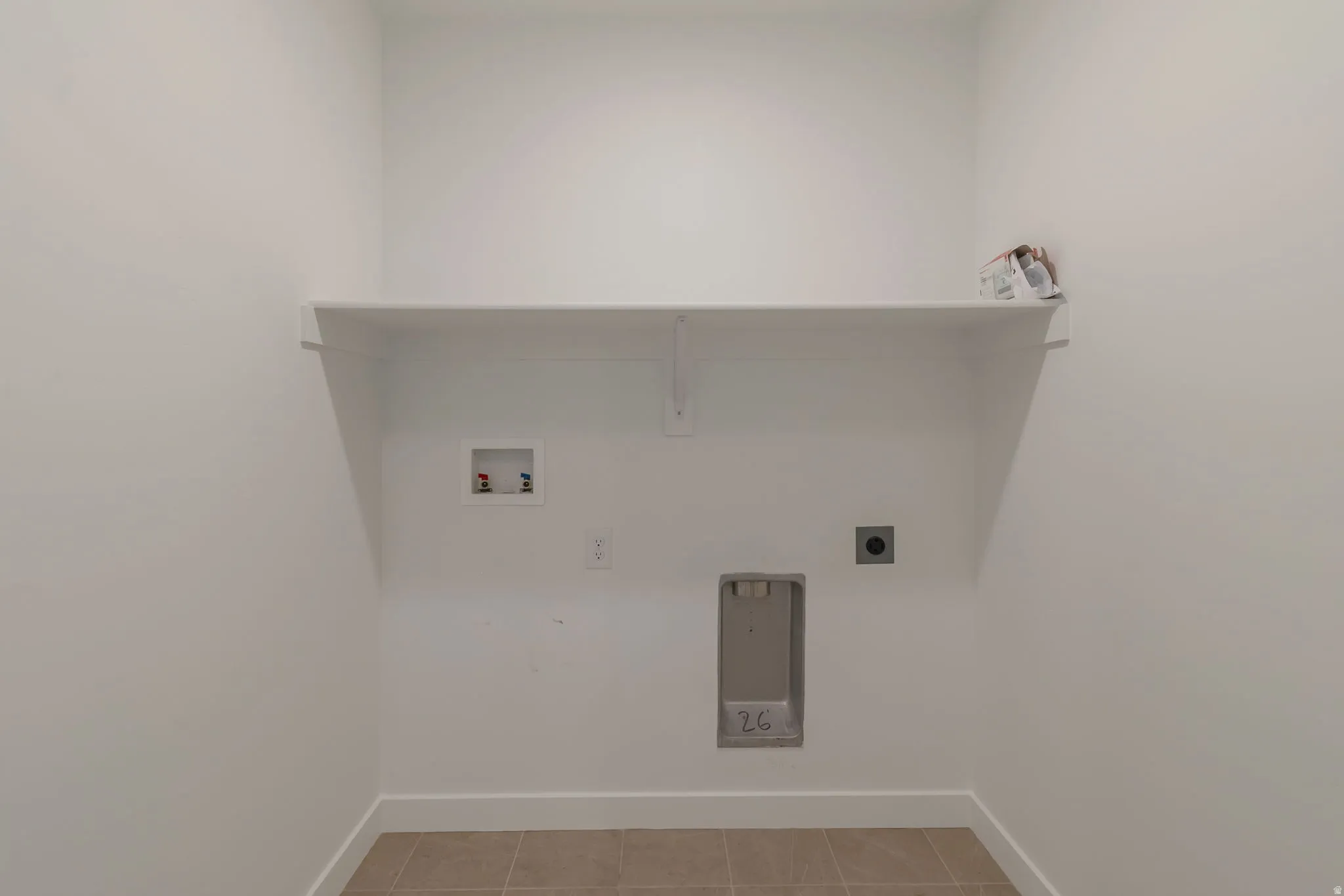 Dedicated laundry area with a wide built-in shelf, plumbing hookups, electrical outlet, and neutral-toned tile flooring