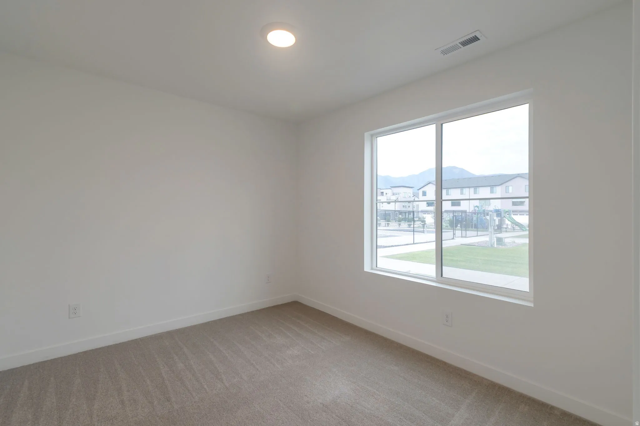 Spacious room featuring neutral carpeting, white walls, a large window, a ceiling-mounted light fixture, and baseboard trim