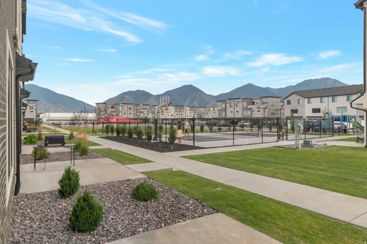 Community recreation area featuring a fenced sports court, expansive green space, and mature landscaping
