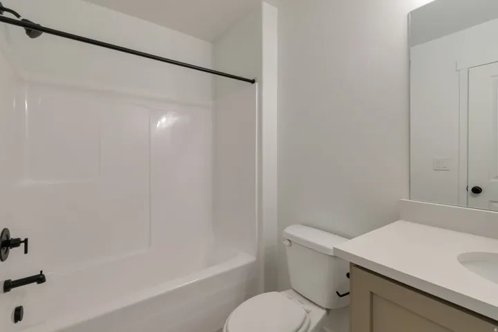 Bathroom featuring a white tub/shower combination with matte black fixtures, a white toilet, and a vanity with a light-colored countertop and a light brown base
