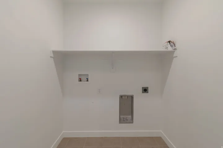 Dedicated laundry area with a wide built-in shelf, plumbing hookups, electrical outlet, and neutral-toned tile flooring