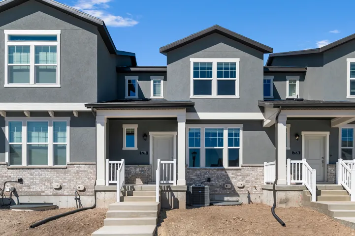 Modern townhouse exterior featuring stucco siding, brick veneer accent, white trim, covered entry, and individual concrete steps