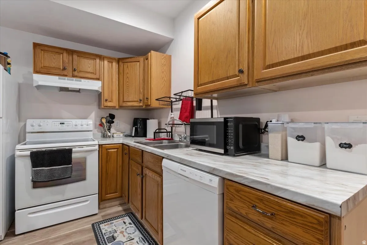 Kitchen featuring wood-finish cabinetry, white appliances, and a light-toned countertop