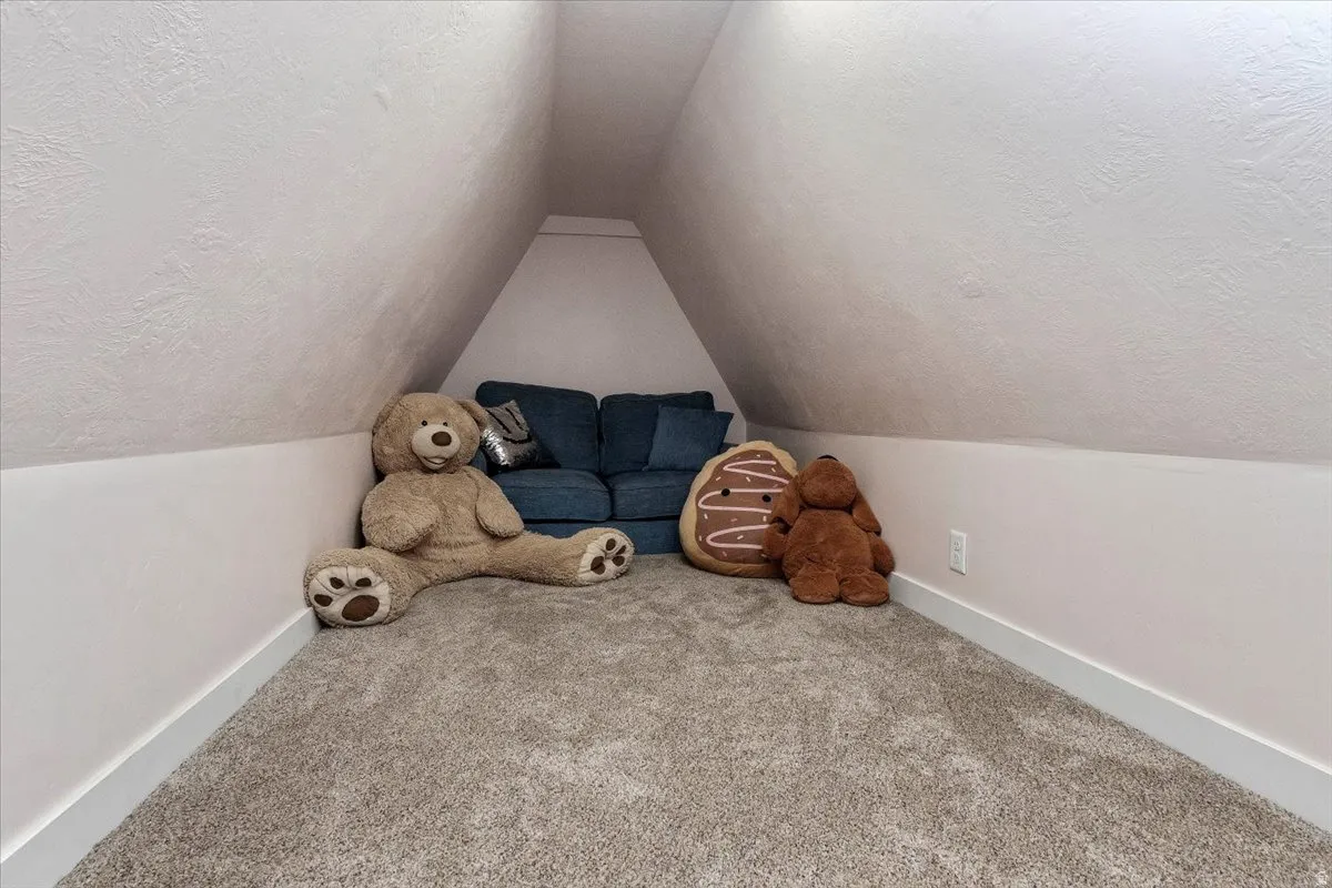 Carpeted attic space featuring sloped ceilings and white baseboards