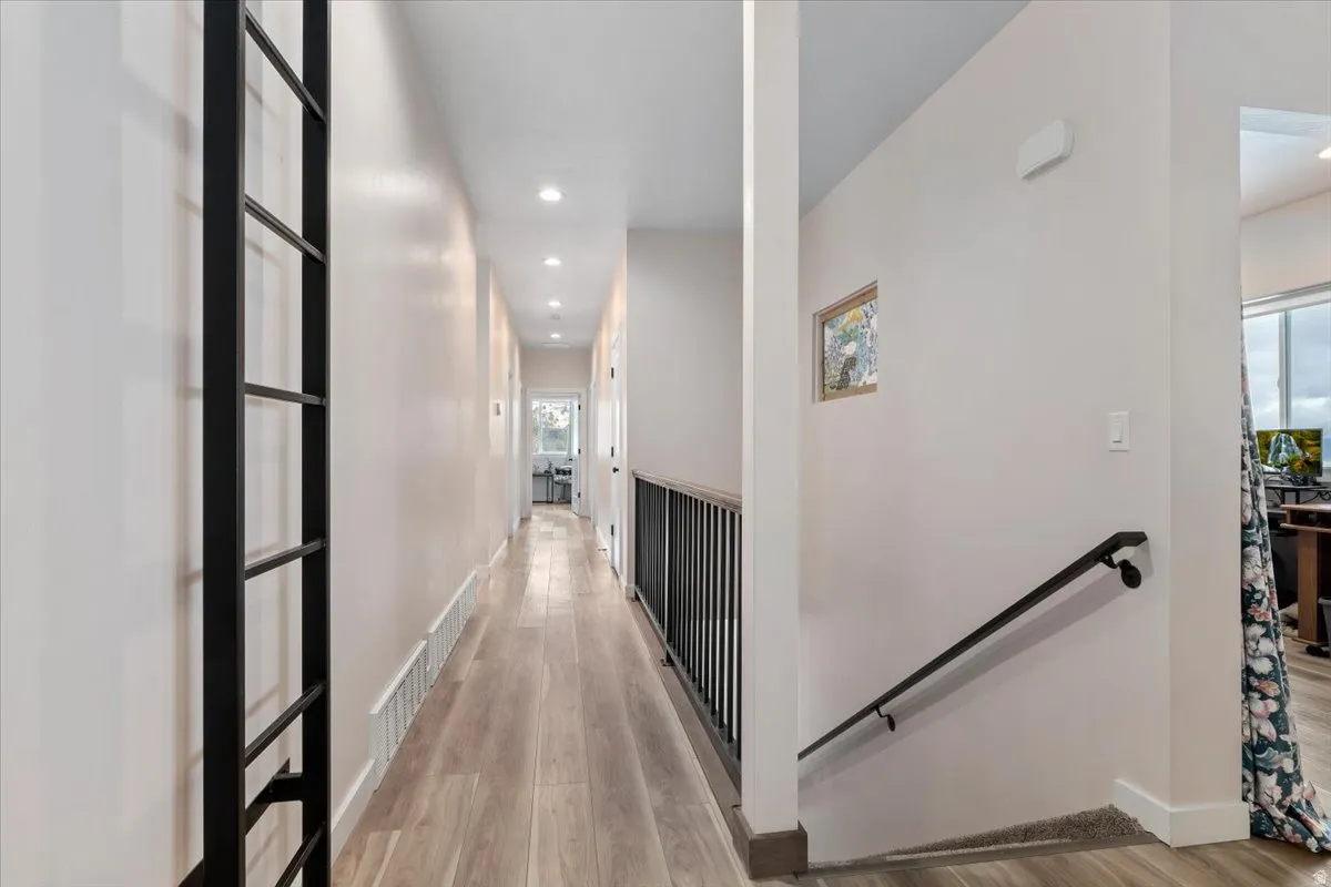 Hallway featuring wood-finish flooring, recessed lighting, and a contemporary black metal railing