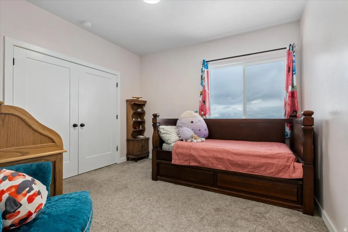 Bedroom featuring light-colored walls, broad window with dark-toned frame, and light gray carpeted flooring