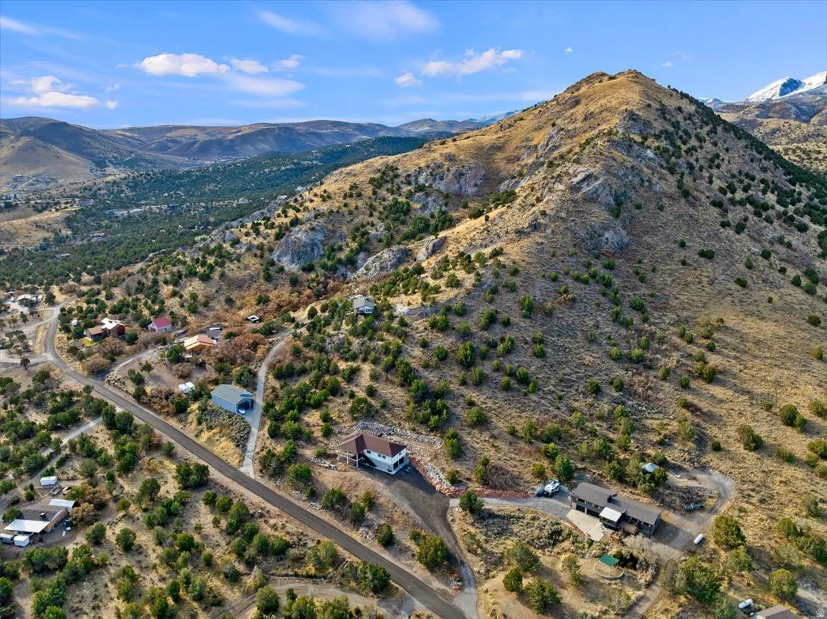 Mountainous terrain property featuring a two-story residence with an attached garage, a paved driveway, and surrounding natural landscaping