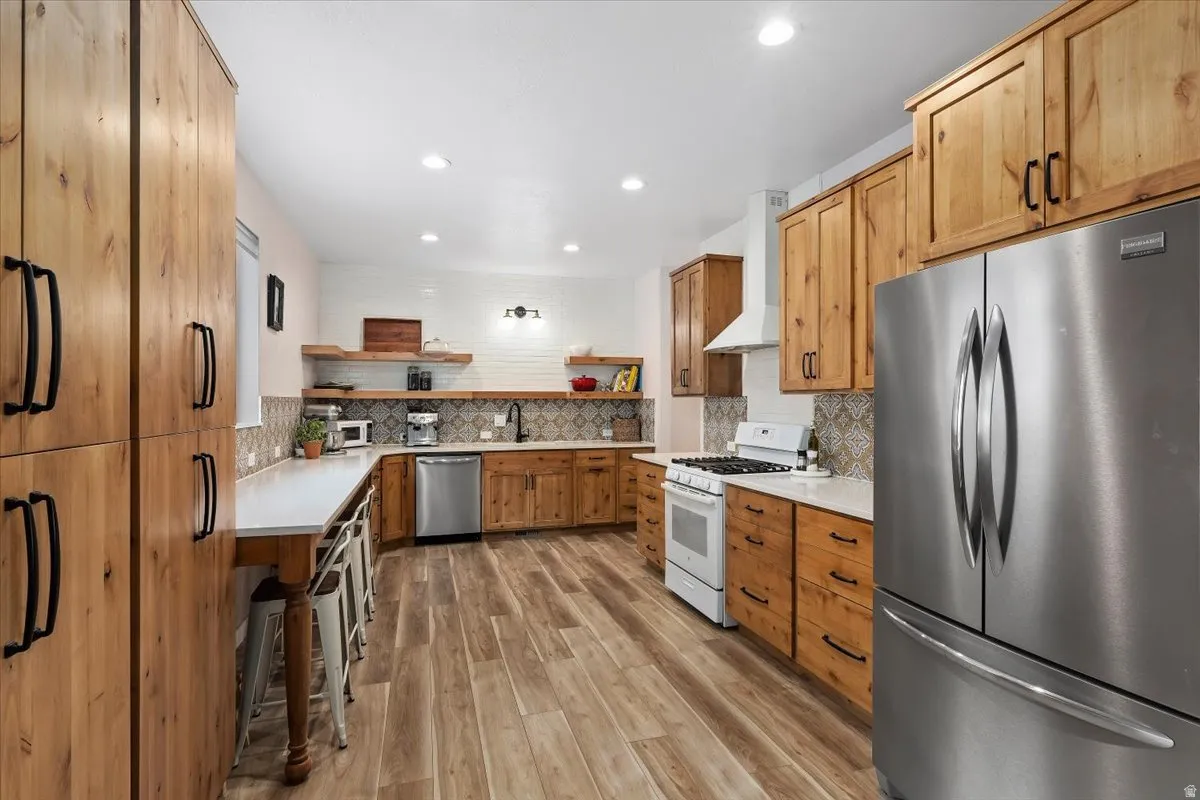 Spacious kitchen featuring extensive wood cabinetry, wood-finish flooring, a stainless steel refrigerator, white countertops, and a decorative tile backsplash