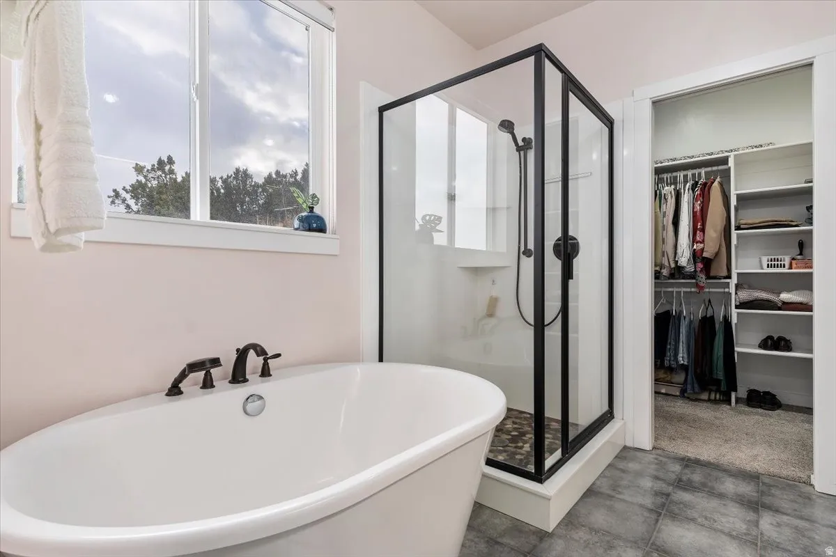 Freestanding soaking tub with dark bronze fixtures, glass-enclosed shower with dark bronze hardware, and tile flooring