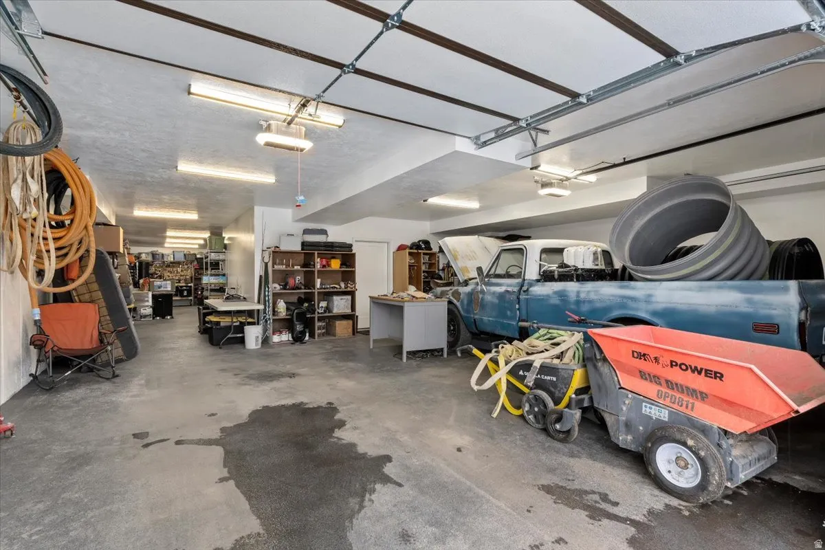 Spacious garage featuring a concrete floor, exposed beam ceiling, and multiple fluorescent light fixtures