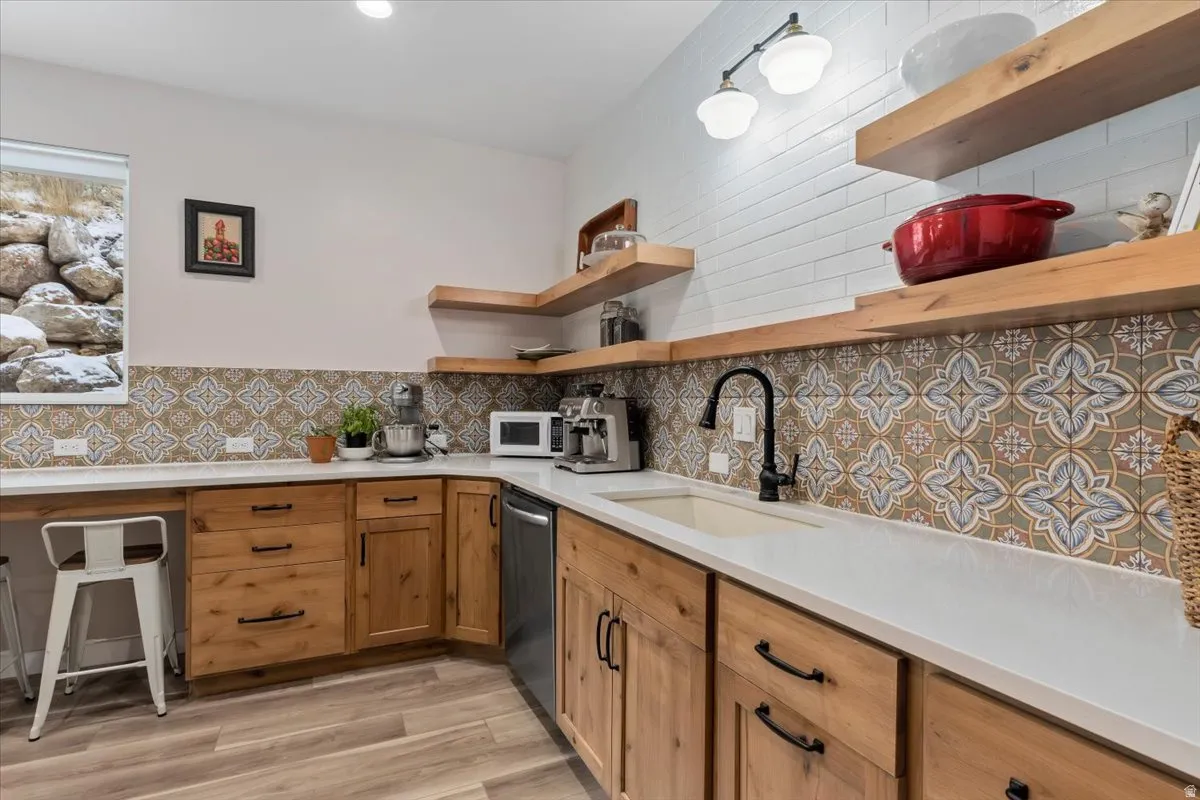 Kitchenette featuring wood-finish flooring, light wood cabinetry with dark hardware, solid surface countertops, and a patterned tile backsplash