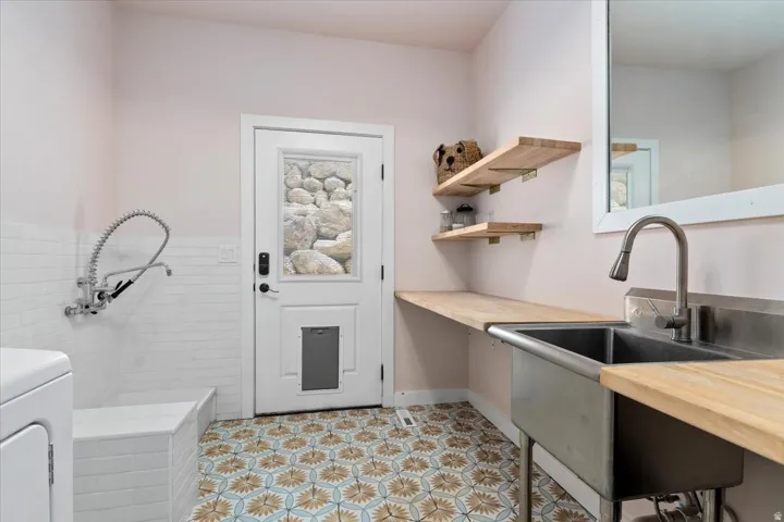Utility room featuring patterned floor tiles, a built-in wash basin with wall-mounted faucet, and a large stainless steel utility sink with wood-finish countertops