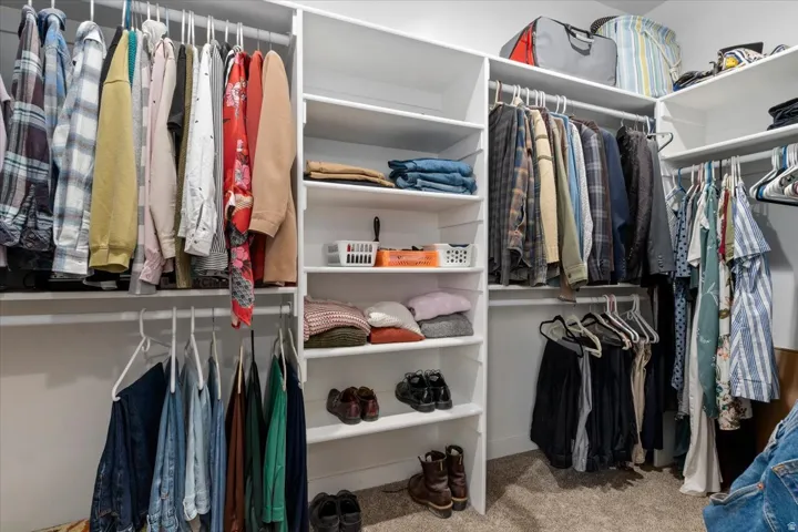 Built-in closet system featuring multiple hanging rods, white shelving, and carpet flooring