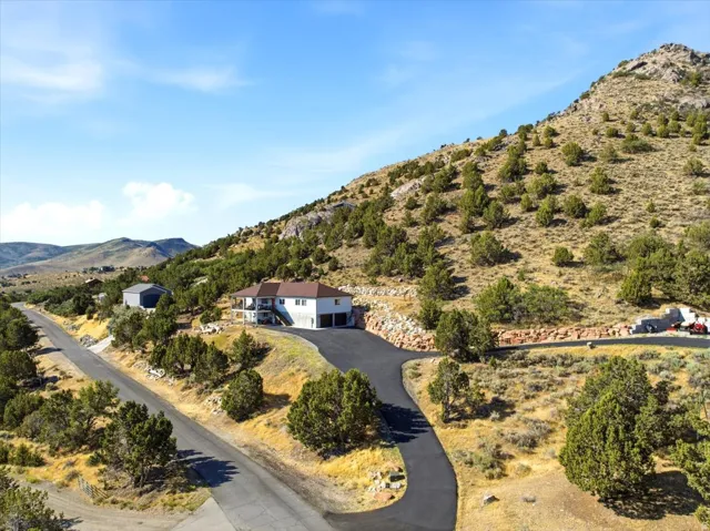 Residence featuring a covered balcony, attached garage, and paved driveway, positioned on a hillside with natural landscaping and a detached auxiliary building