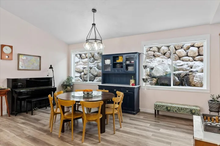 Dining area featuring wood-finish flooring, a contemporary chandelier, two windows with rock garden views, and a prominent built-in hutch