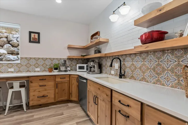 Kitchenette featuring wood-finish flooring, light wood cabinetry with dark hardware, solid surface countertops, and a patterned tile backsplash