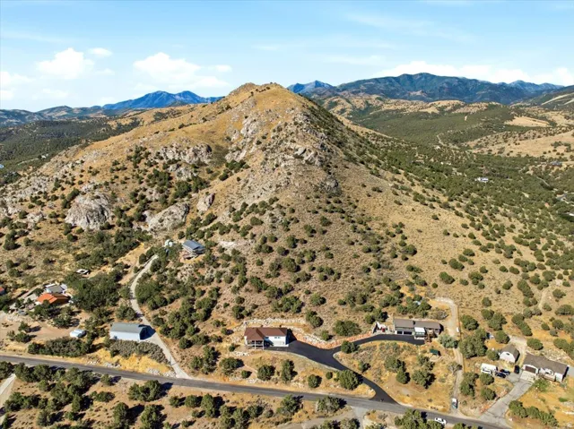Expansive property set amidst mountainous terrain and natural vegetation, featuring a paved driveway and surrounding residential structures
