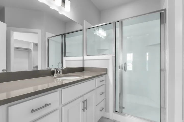 White vanity with brushed nickel hardware, gray countertop, undermount sink, large mirror, and glass-enclosed shower