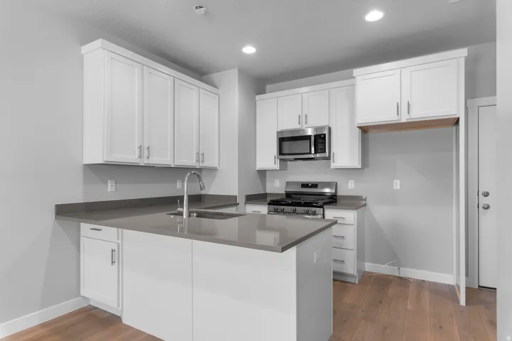 Modern kitchen featuring white shaker cabinetry, stainless steel appliances, a center island with sink, gray countertops, and wood-finish flooring