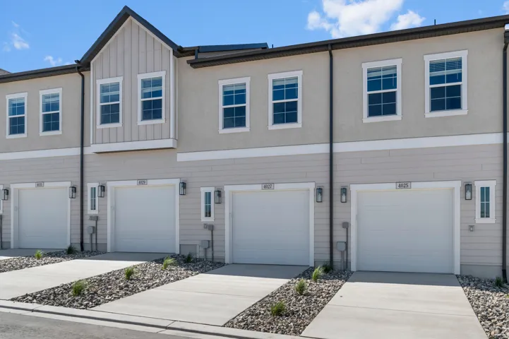 Contemporary townhome exterior featuring an attached garage, concrete driveway, and rock landscaping