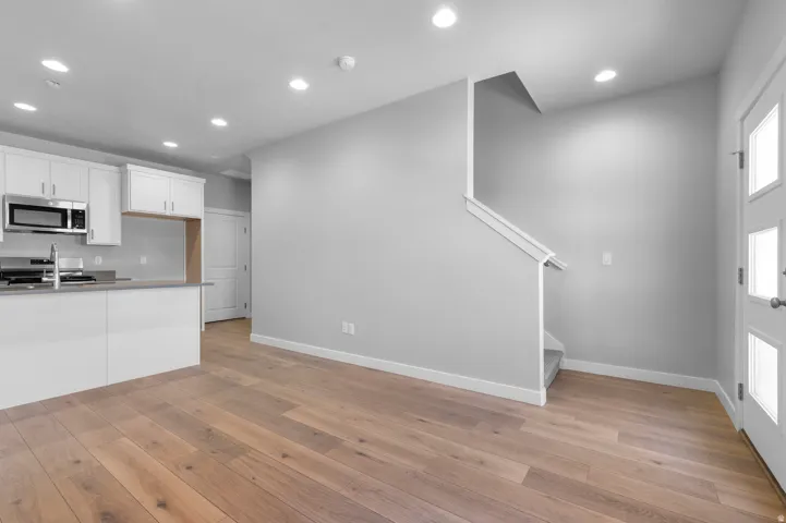 Wood-finish flooring, white cabinetry, integrated stainless steel microwave, staircase with carpeted treads, and recessed ceiling lighting