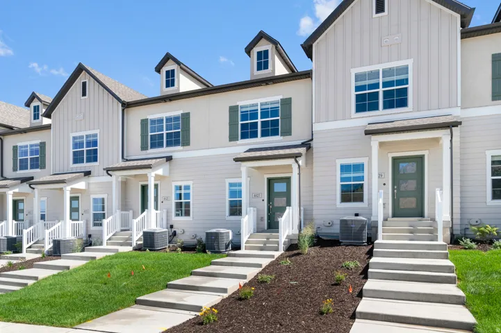 Townhome exterior with light-colored siding, contrasting dark shutters, and a covered porch entry