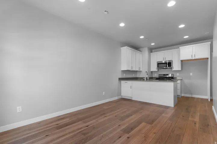 Wood-finish flooring, white cabinetry, stainless steel appliances, recessed lighting, and a kitchen island with a sink