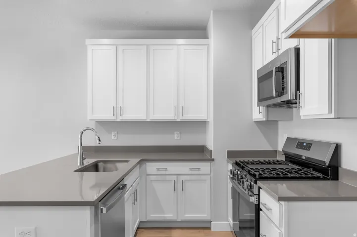 White shaker cabinetry, grey countertops, stainless steel appliances, stainless steel sink, and wood-finish flooring