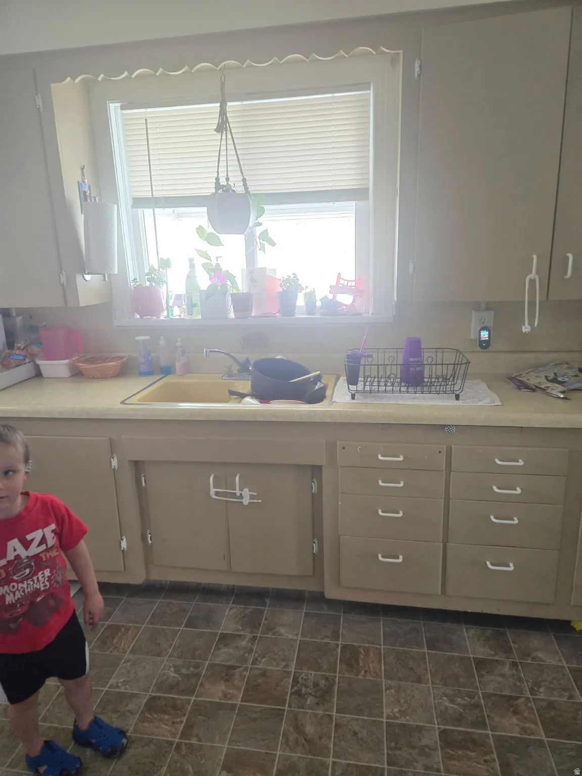 Kitchen featuring a single basin sink, a window with horizontal blinds, upper and lower cabinetry, and tiled flooring