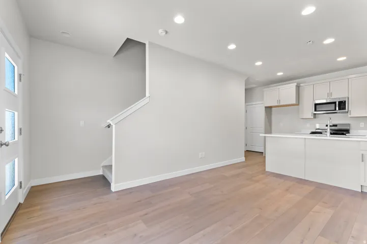 Wood-finish flooring throughout, modern kitchen cabinetry with stainless steel appliances, recessed lighting, white quartz countertops, and a contemporary entry door with frosted glass panels