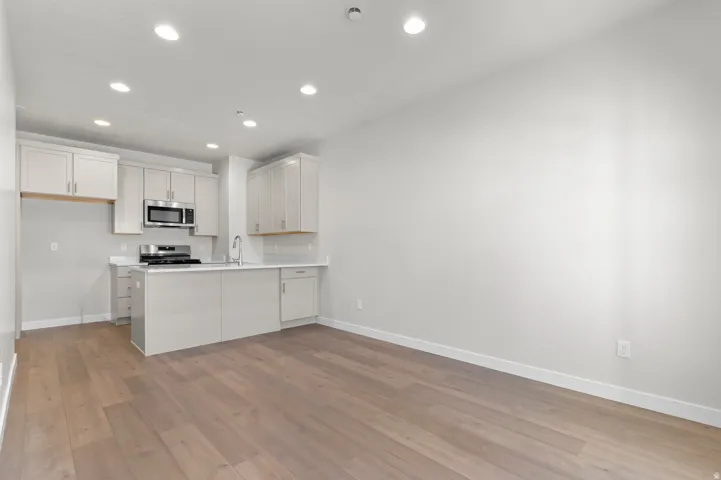 Open concept living space featuring wood-finish flooring, recessed lighting, a kitchen island, stainless steel appliances, and light-toned cabinetry