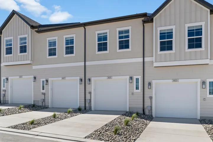 Modern townhome exterior featuring light-colored siding, multiple windows, attached garages, and concrete driveways with rock accents