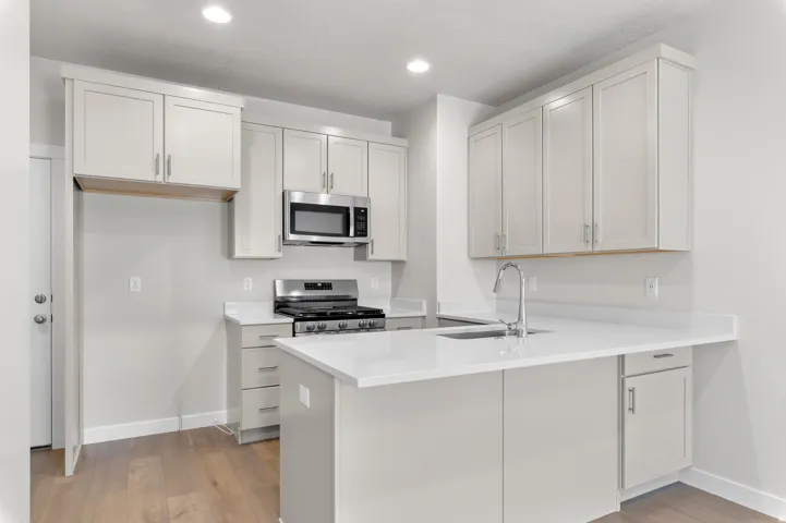 Modern kitchen featuring light-toned cabinetry, stainless steel appliances, a center island with a sink, white countertops, and wood-finish flooring