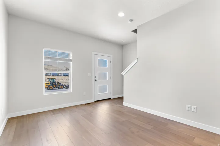 Light wood-finish flooring, recessed ceiling lighting, a modern entry door with frosted glass panels, and a painted handrail along the staircase