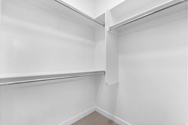 Walk-in closet featuring white painted walls, built-in shelving, and metal hanging rods