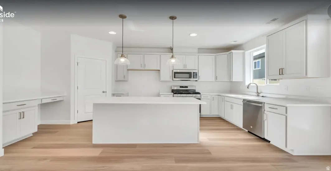 Contemporary kitchen featuring white cabinetry, a center island, stainless steel appliances, and wood-finish flooring. This home is under construction, the pictures are of a similar home