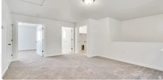 Spacious carpeted bonus room featuring neutral wall tones, multiple doorways, a half-wall partition, and ceiling-mounted lighting. This home is under construction, the pictures are of a similar home