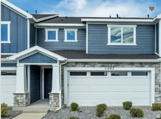 Modern townhome exterior featuring blue horizontal siding, a stone veneer facade, a covered entry with stone-clad columns, a two-car garage with transom windows, and white trim accents. This home is under construction, and pictures are of a similar home.