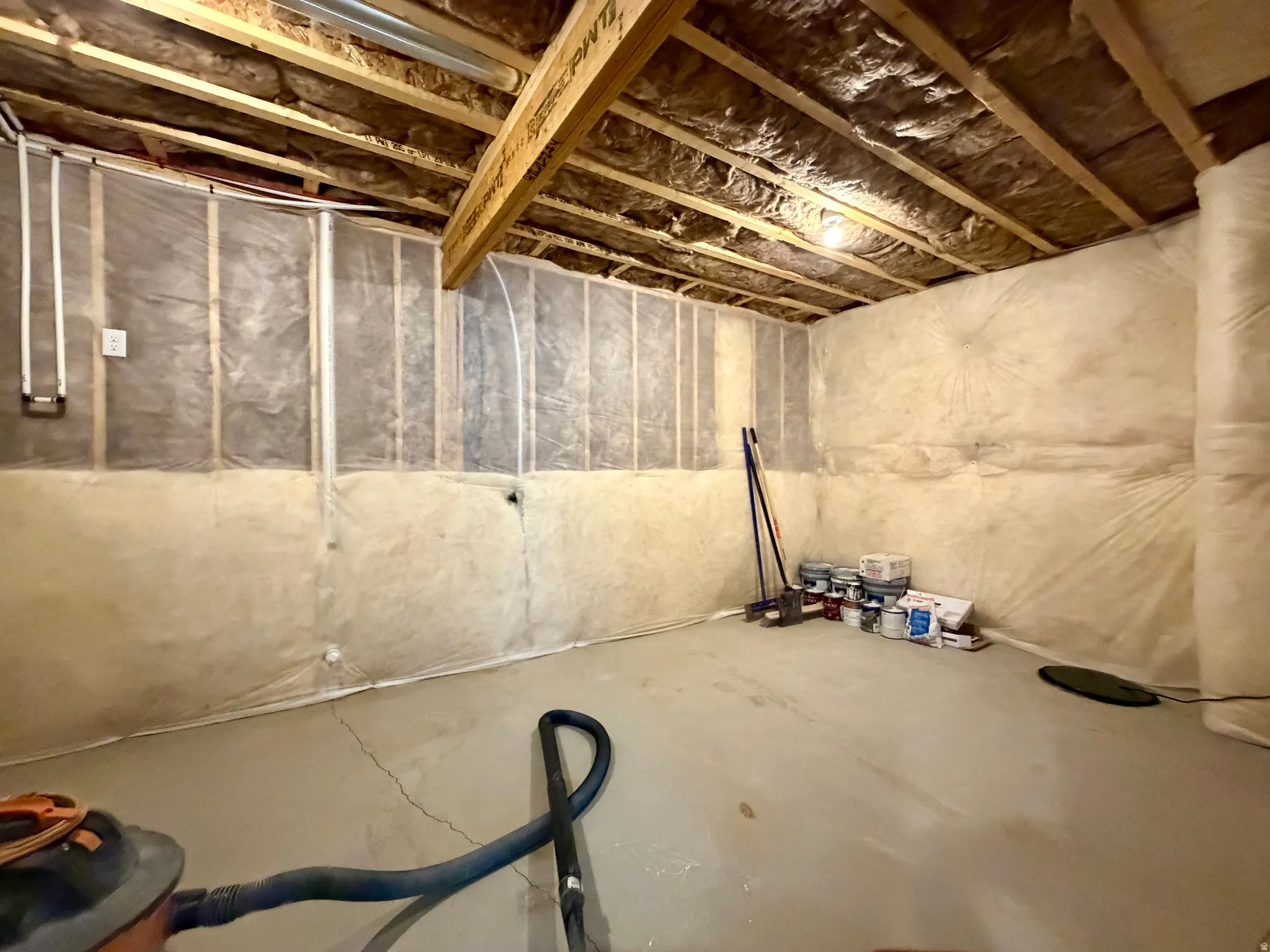 Unfinished basement space featuring exposed wooden ceiling joists, insulated walls, and a concrete floor