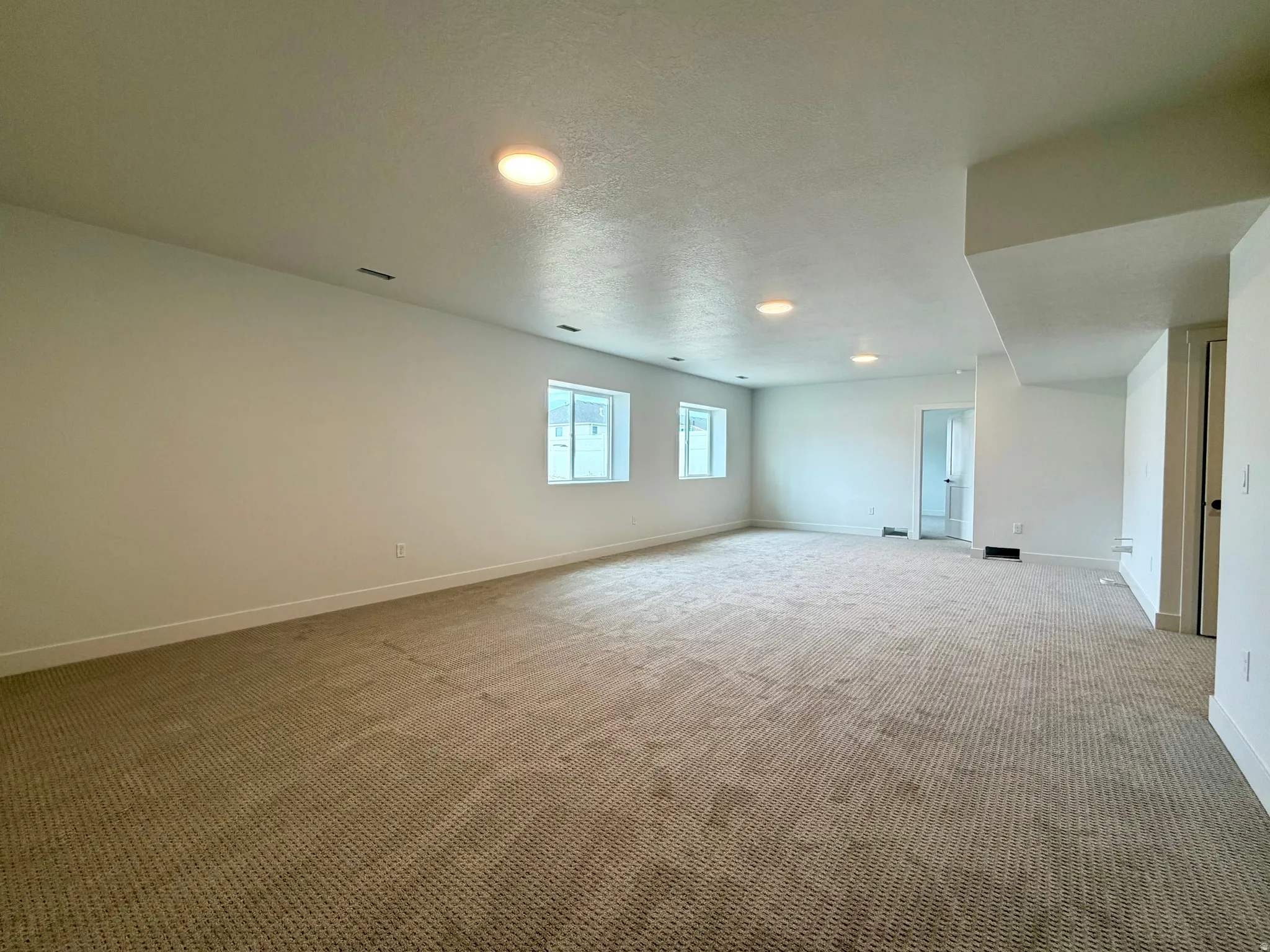 Spacious room featuring neutral carpeting, recessed ceiling lighting, and multiple windows providing natural light