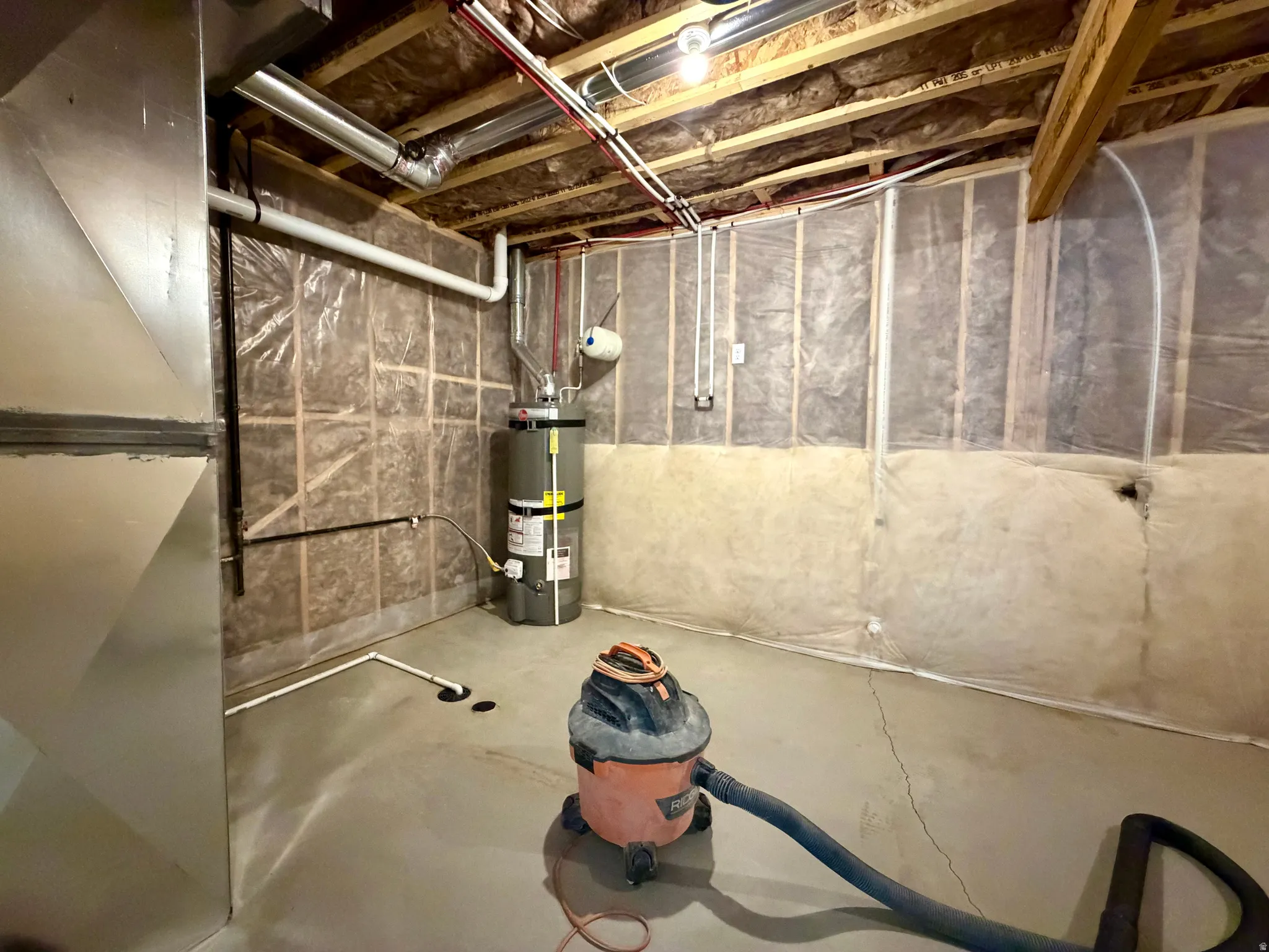 Unfinished basement with concrete flooring, exposed wood ceiling joists, and visible insulation