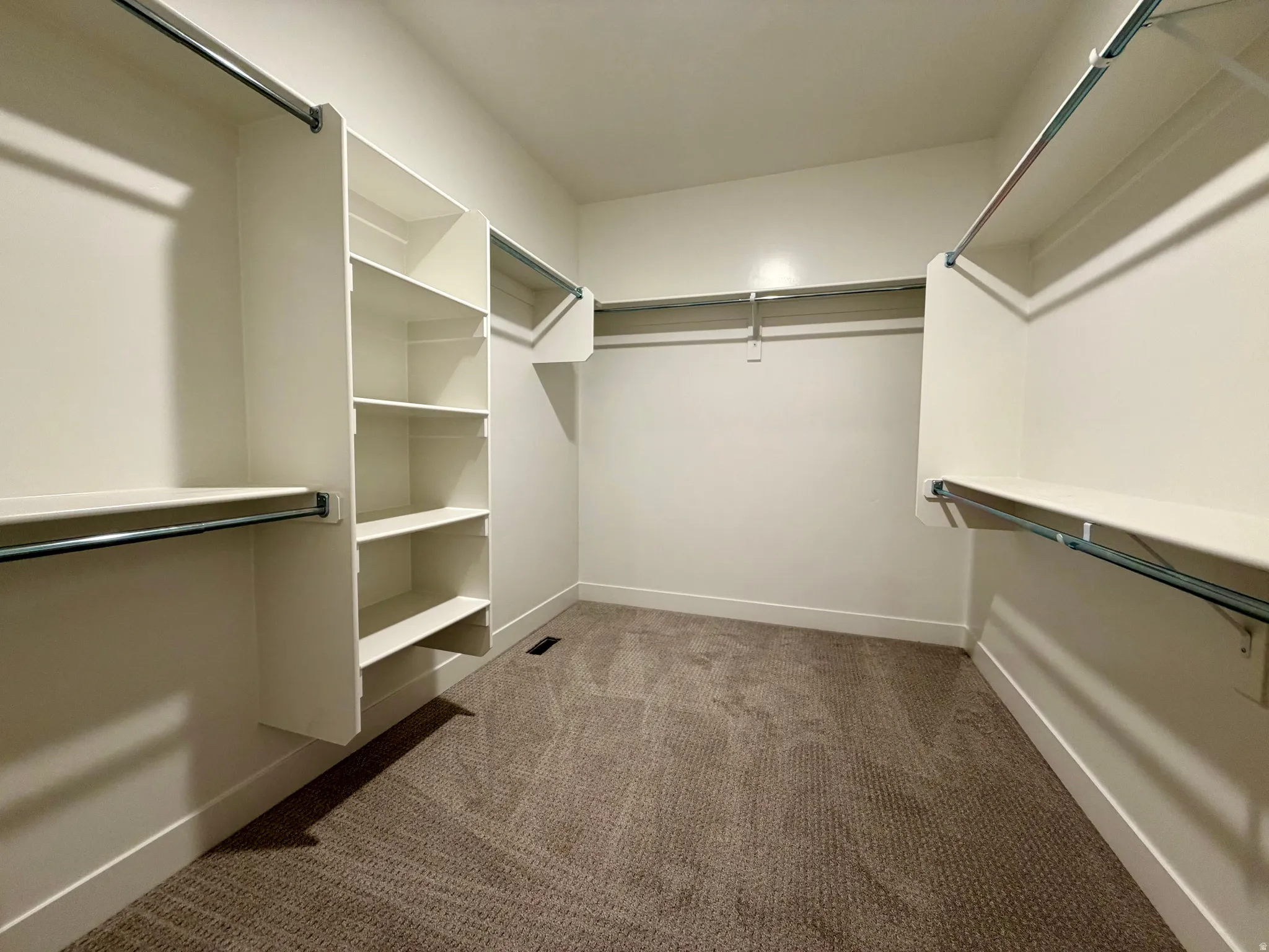 Spacious walk-in closet featuring built-in shelving, multiple hanging rods, white walls, white baseboards, and brown patterned carpeting