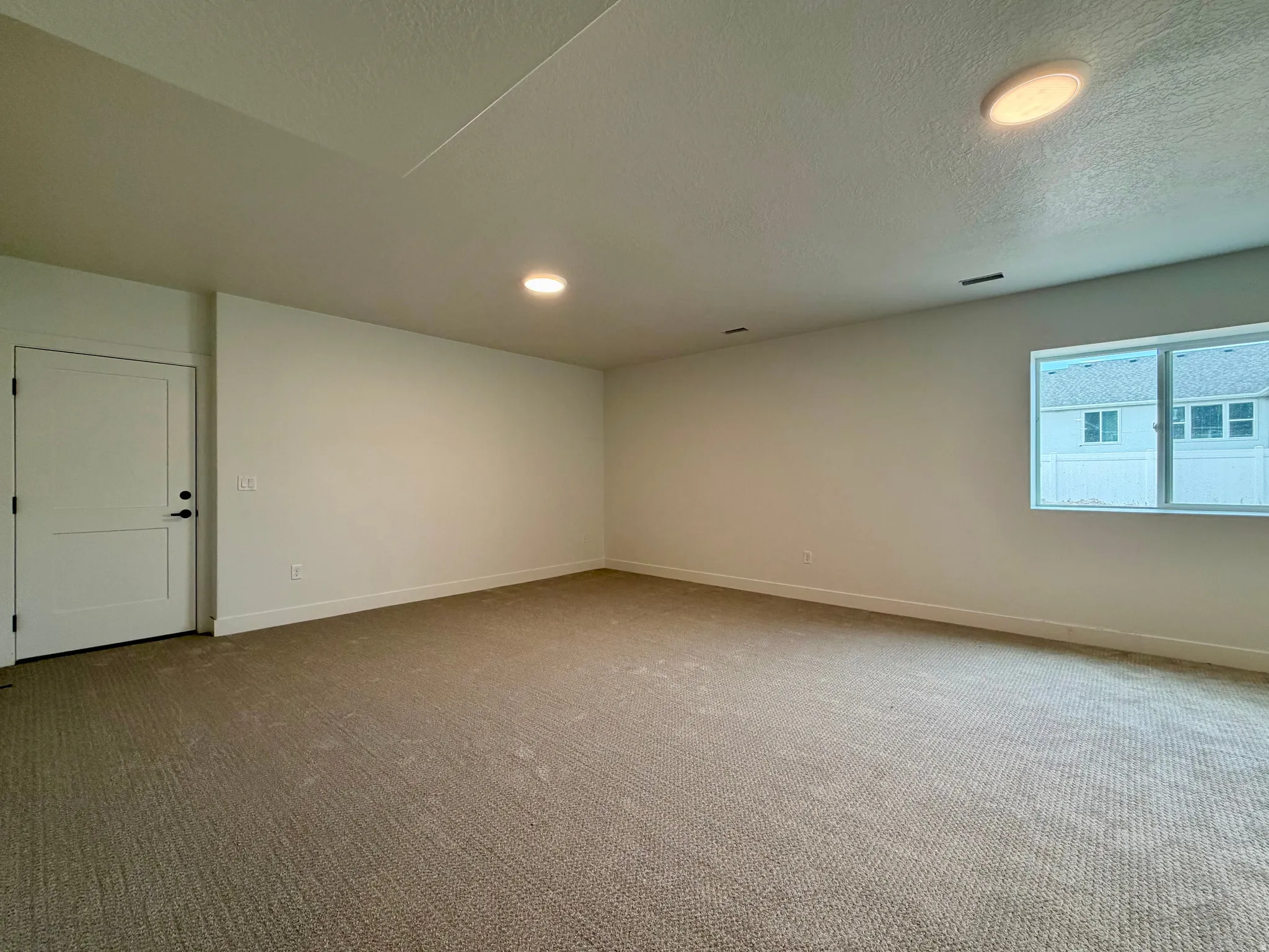Spacious room featuring neutral carpeting, white walls, and a white two-panel interior door with matte black hardware