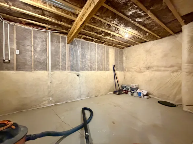 Unfinished basement space featuring exposed wooden ceiling joists, insulated walls, and a concrete floor