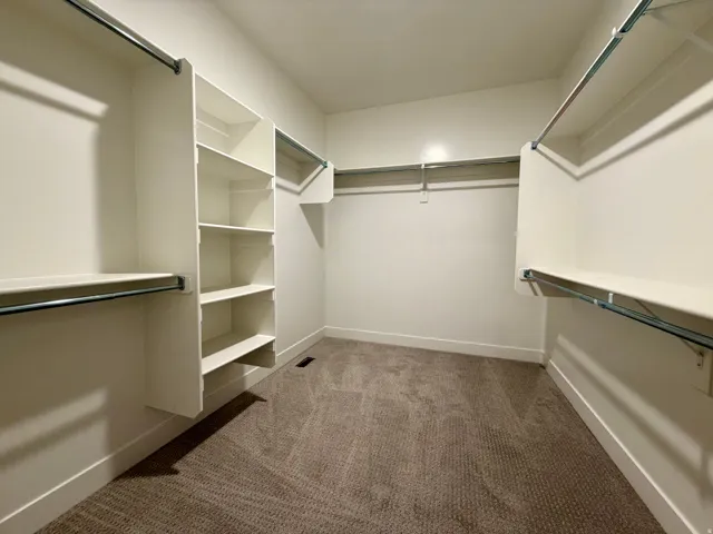 Spacious walk-in closet featuring built-in shelving, multiple hanging rods, white walls, white baseboards, and brown patterned carpeting