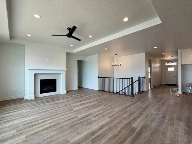 Spacious living area featuring wood-finish flooring, a white mantel fireplace with a tile surround, and a ceiling fan