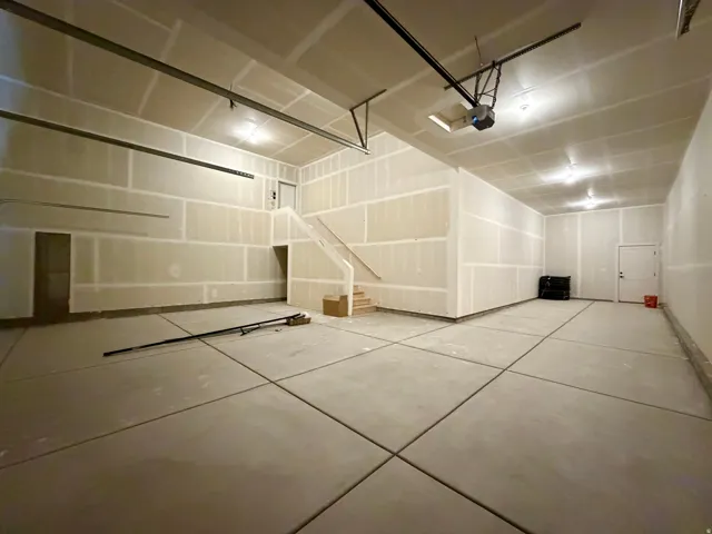 Spacious garage featuring concrete flooring, unpainted drywall, and a visible staircase