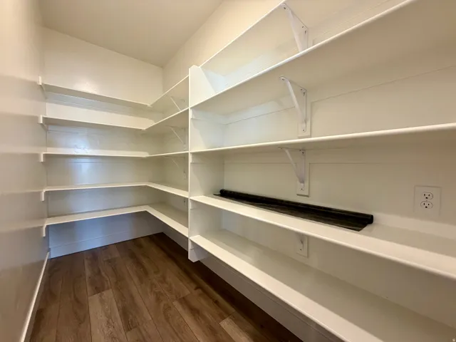 Corner pantry featuring built-in shelving, wood-finish flooring, and wall-mounted electrical outlets