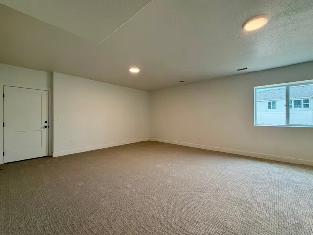 Spacious room featuring neutral carpeting, white walls, and a white two-panel interior door with matte black hardware