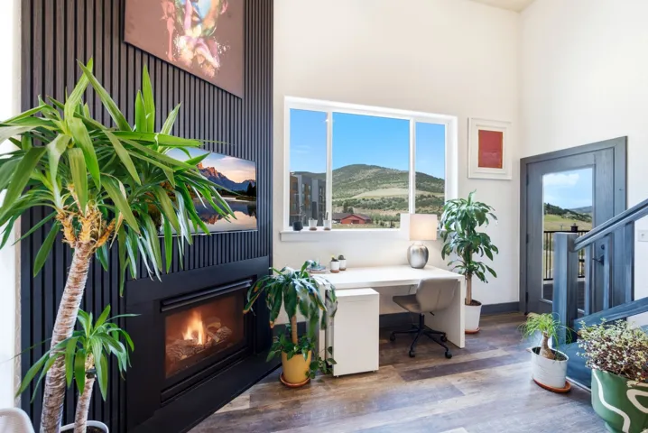 Spacious interior featuring a contemporary fireplace with a black slatted accent wall, high ceilings, a large window, and wood-finish flooring
